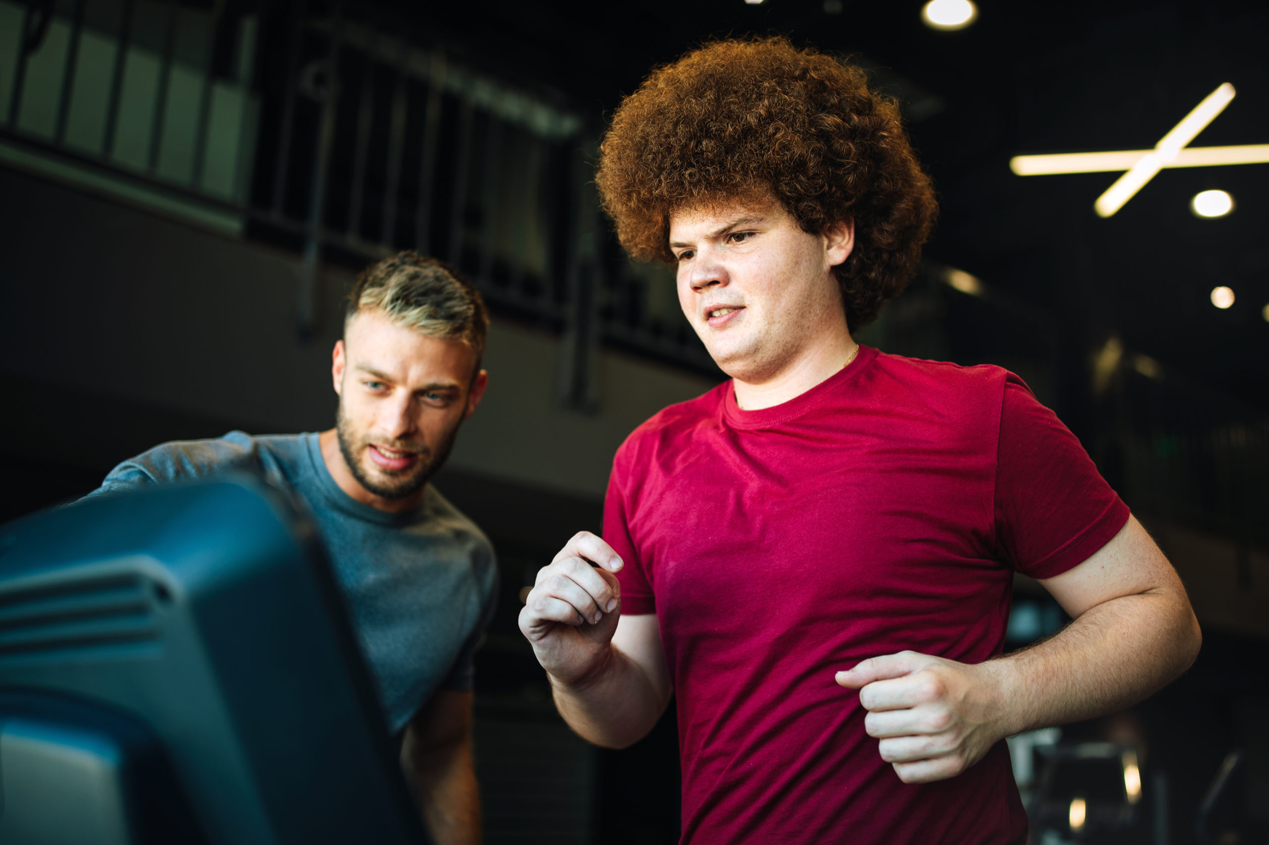 Overweight young chubby man exercising gym with personal trainer